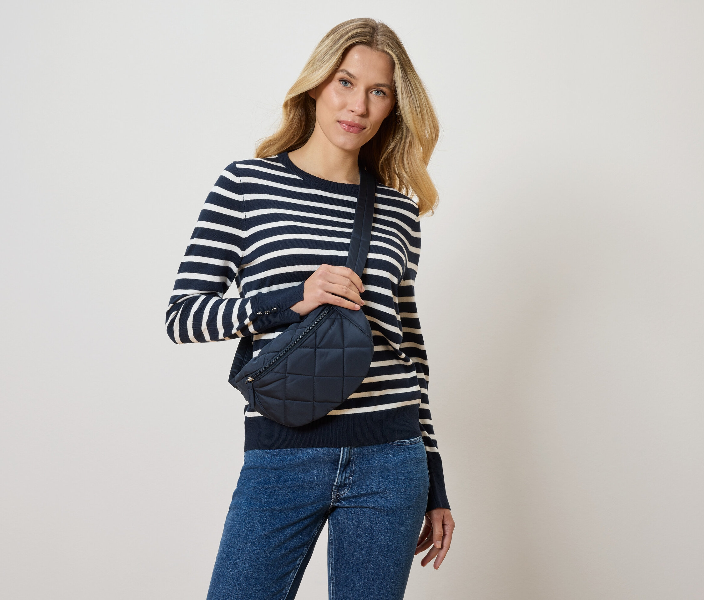 Blonde Frau mit blau-weiß gestreiftem Pullover und blauen Jeans, die eine marineblaue Gürteltasche trägt.
