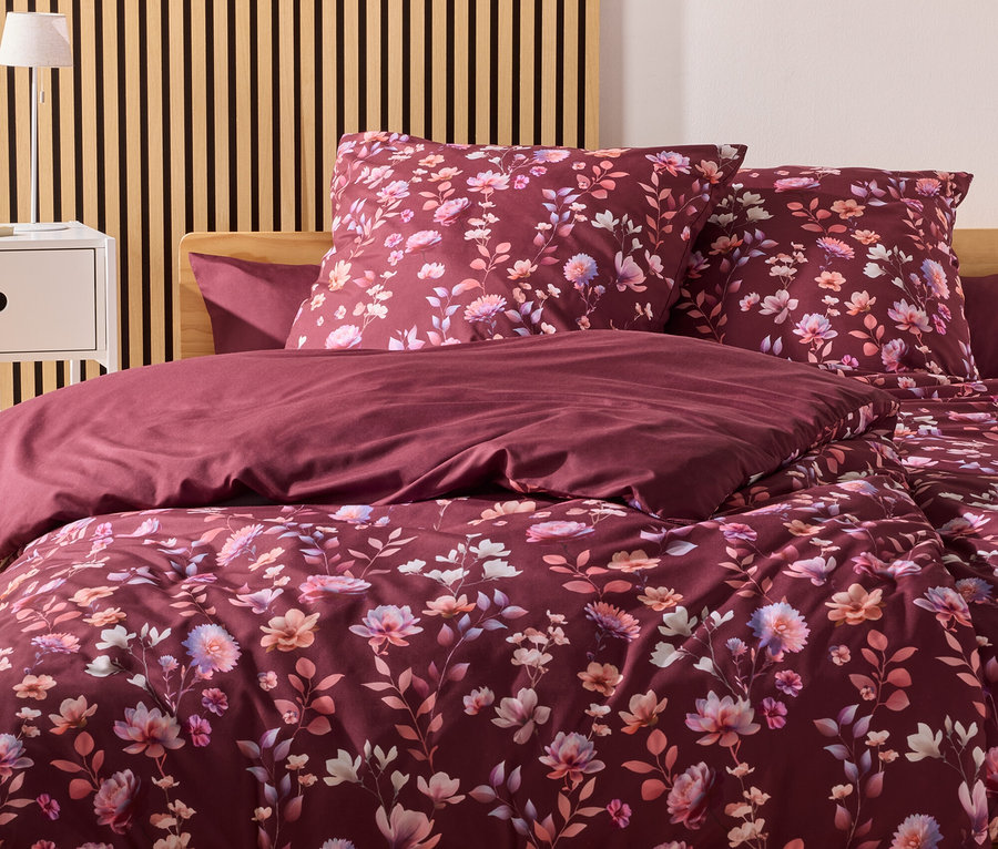 Burgunderfarbene Bettwäsche mit Blumenmuster liegt auf einem Bett mit Holzkopfende vor einer Wand mit Holzpaneelen.