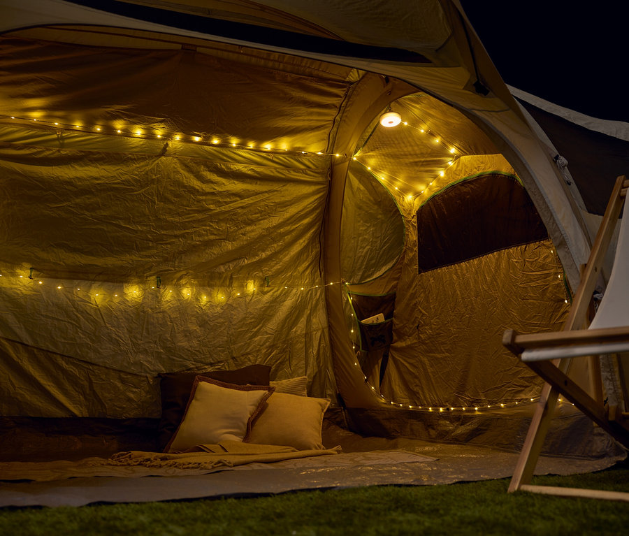 Blick ins Innere eines Zeltes mit Lichterketten, Kissen und einer Decke.