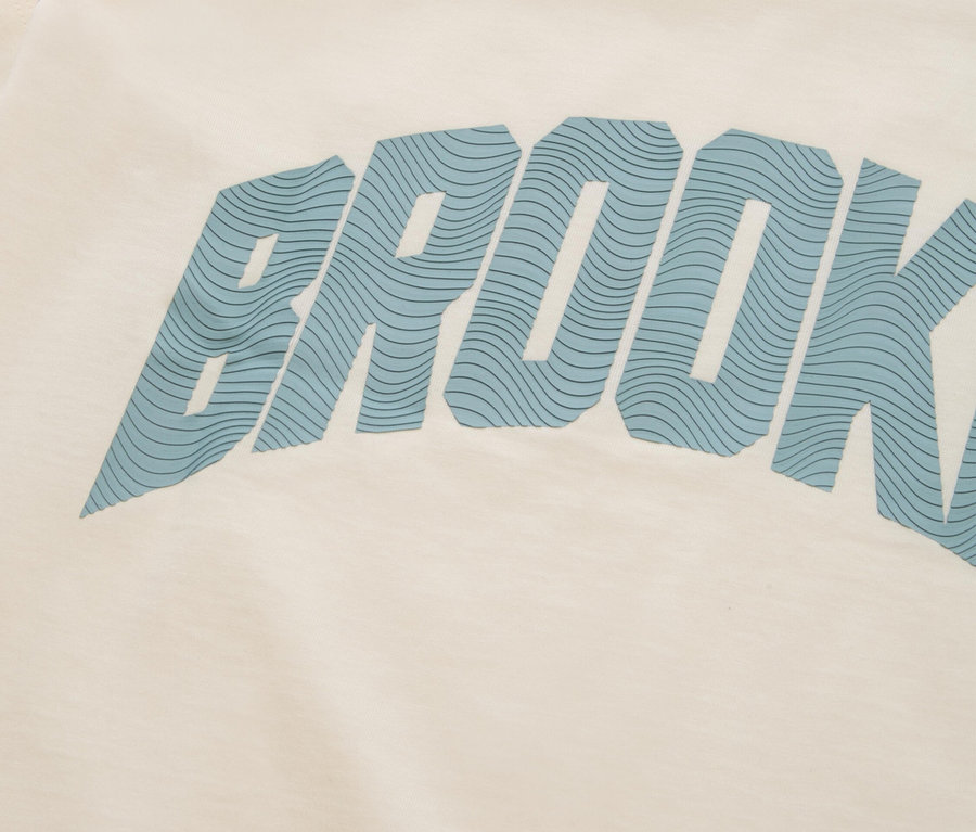 Nahaufnahme eines cremefarbenen T-Shirts mit blauem Schriftzug „BROOKLYN“.