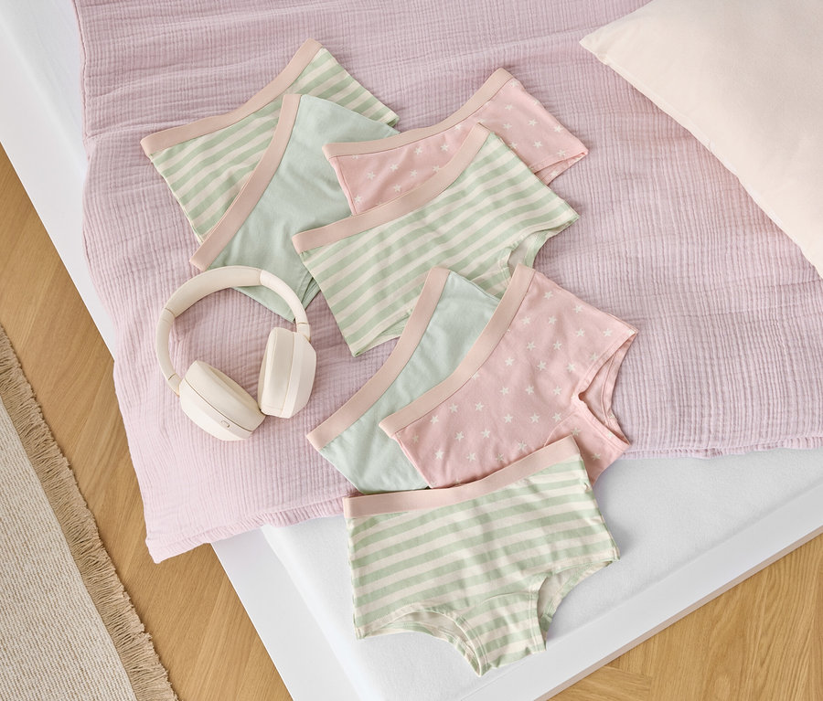 Auf einem Bett liegen Baumwollslips mit Streifen- und Sternmuster neben weißen Kopfhörern.