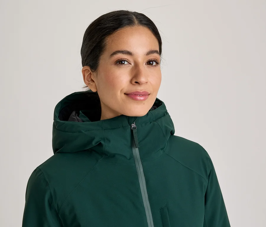Lächelnde Frau in einer dunkelgrünen Kapuzenjacke, die direkt in die Kamera blickt.
