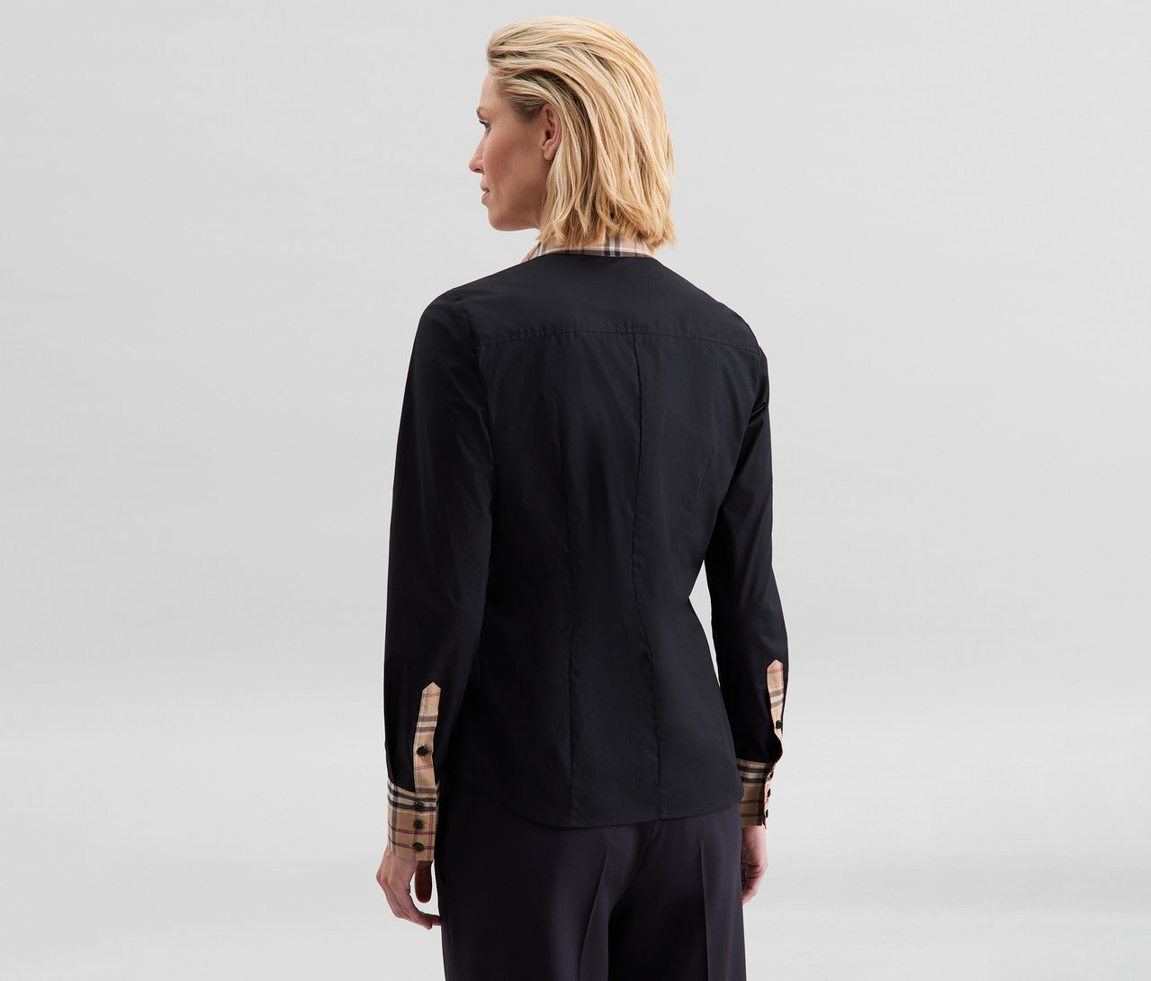 Frau von hinten, trägt eine schwarze Seidensticker Popeline-Bluse mit Karodetail am Kragen und an den Manschetten.
