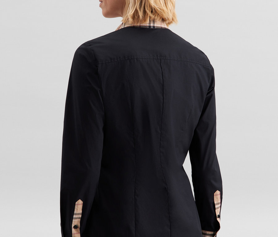 Frau von hinten, trägt eine schwarze Seidensticker Popeline-Bluse mit Karodetail am Kragen und an den Ärmelbündchen.