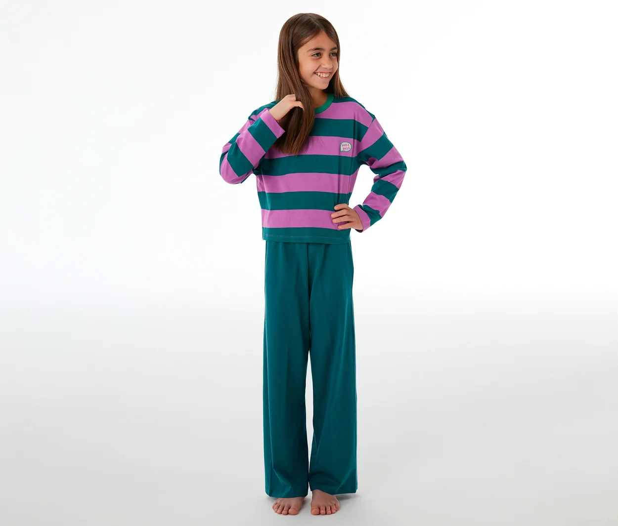Lächelndes Mädchen in einem SCHIESSER Kinder-Pyjama mit lila-grün gestreiftem Oberteil und grüner Hose.