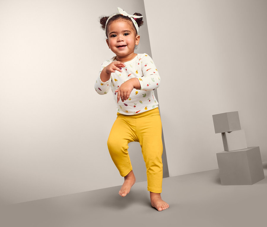 Lächelndes kleines Mädchen tanzt und trägt eine 3-teilige Baby-Kombi.