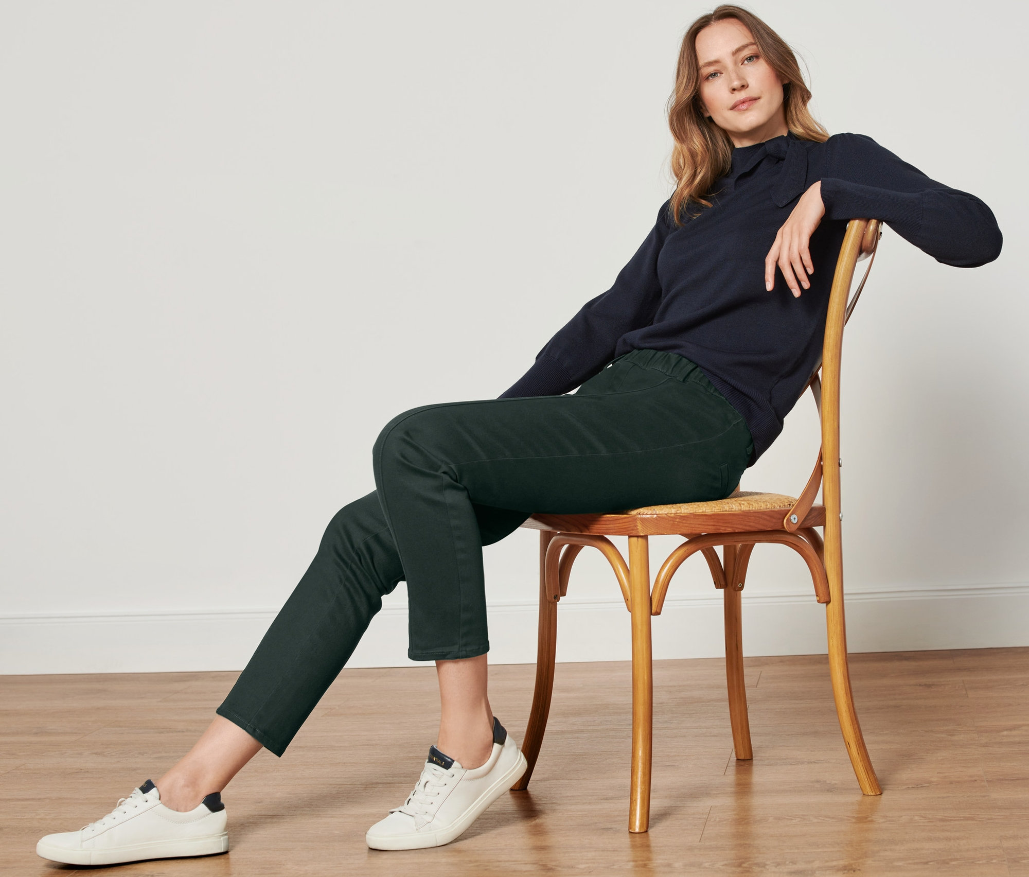 Frau sitzt auf einem Stuhl und trägt eine dunkelgrüne Twillhose mit Komfortbund.