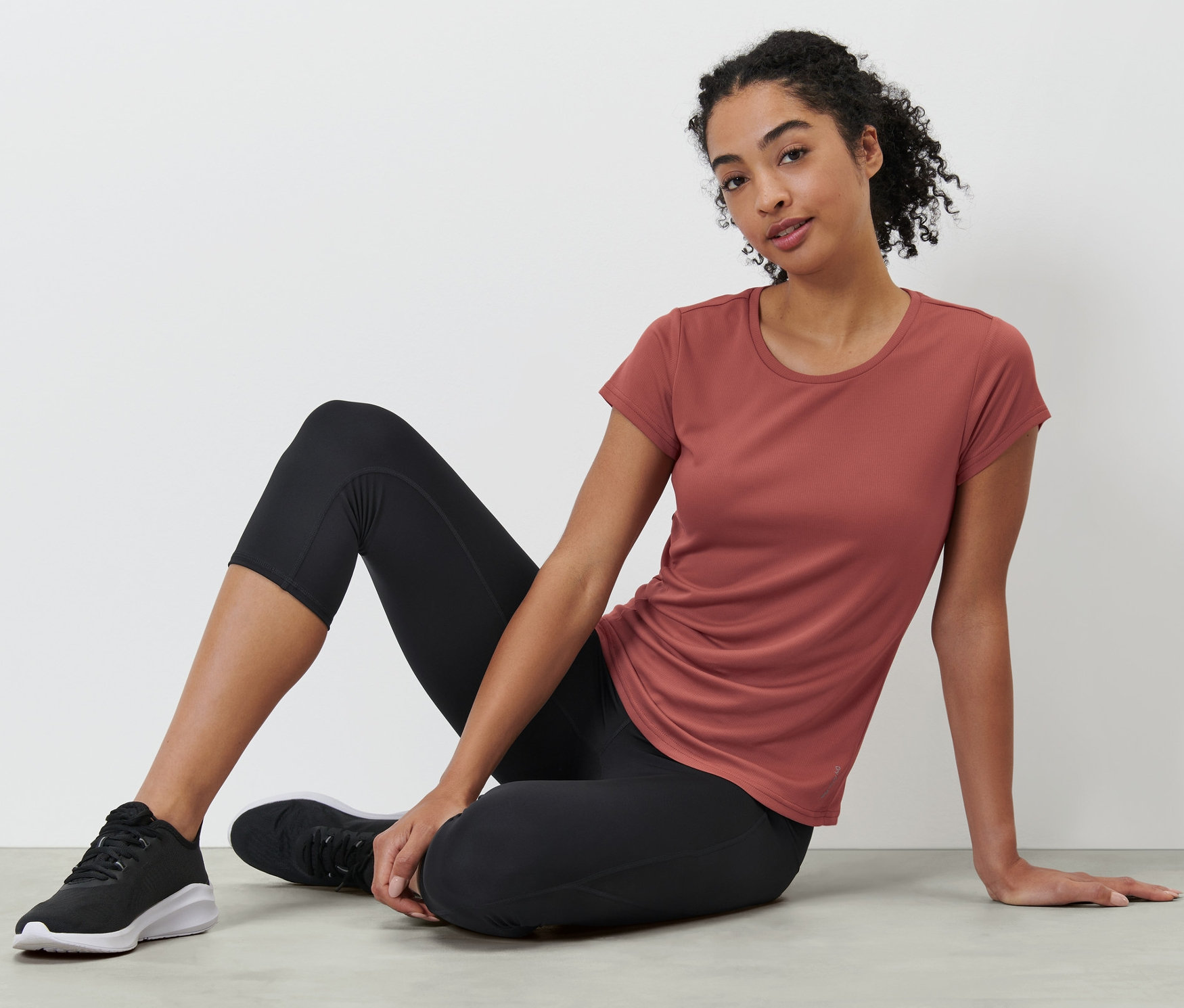 Frau sitzt am Boden und trägt ein terrakottafarbenes Funktionsshirt.