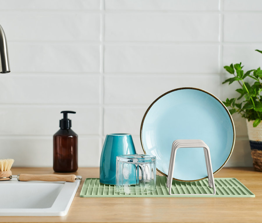 Ein hellgrünes Abtropfgestell mit Silikonmatte, auf dem ein hellblauer Teller, ein Glas und ein Abtropfgestell für Gläser stehen.