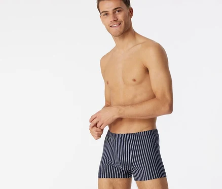 Lächelnder, oberkörperfreier Mann in dunkelblauen SCHIESSER Shorts mit Bio-Baumwolle und weißen Streifen.
