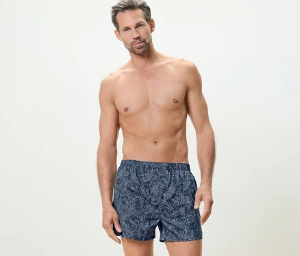 Mann posiert vor hellem Hintergrund und trägt 2 Webboxershorts.