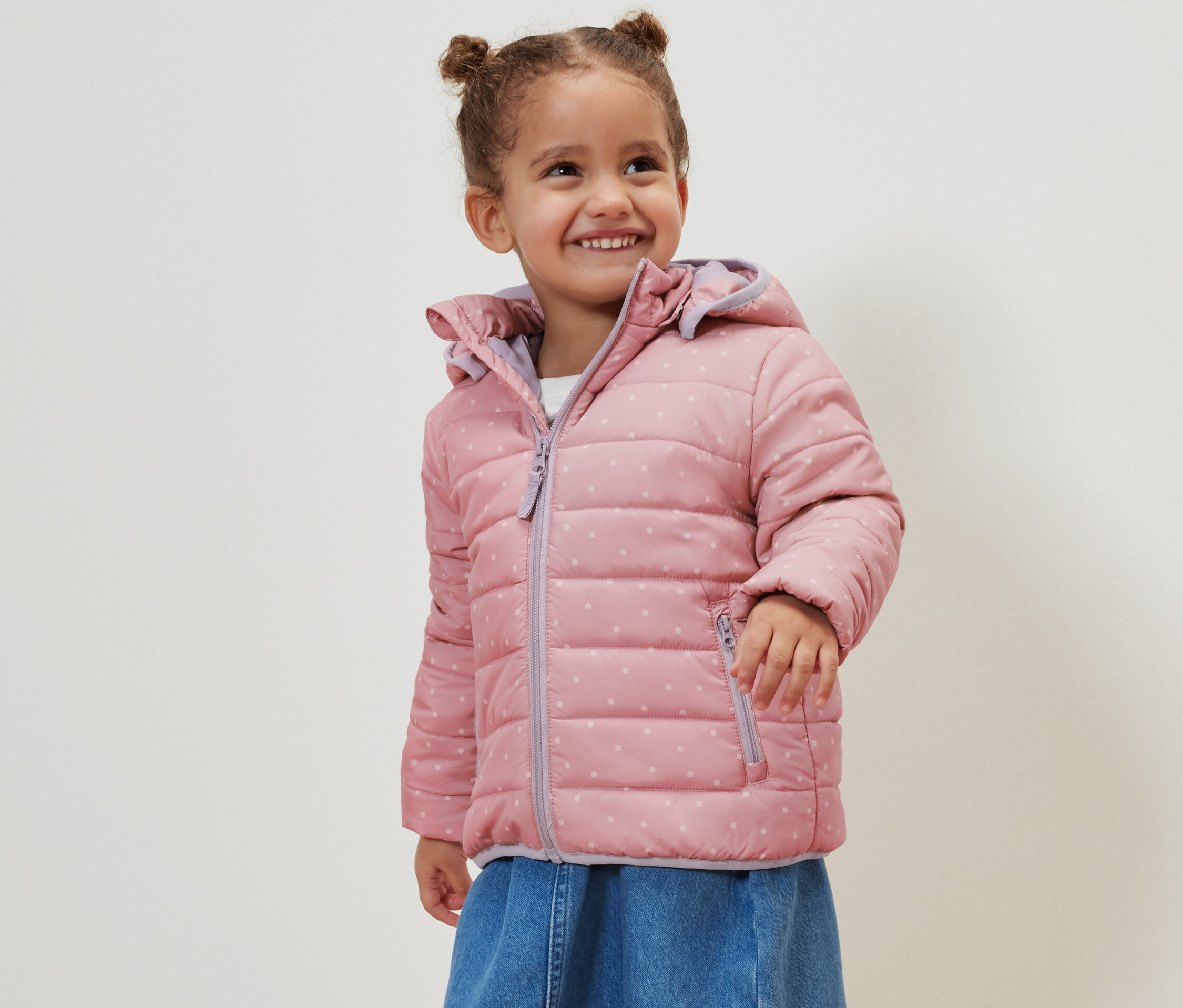 Lächelndes Mädchen trägt eine altrosa Kinder-Steppjacke.