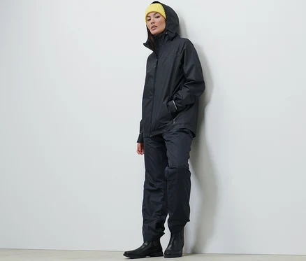 Frau trägt eine dunkelblaue Unisex Regenjacke, Hose und eine gelbe Mütze.