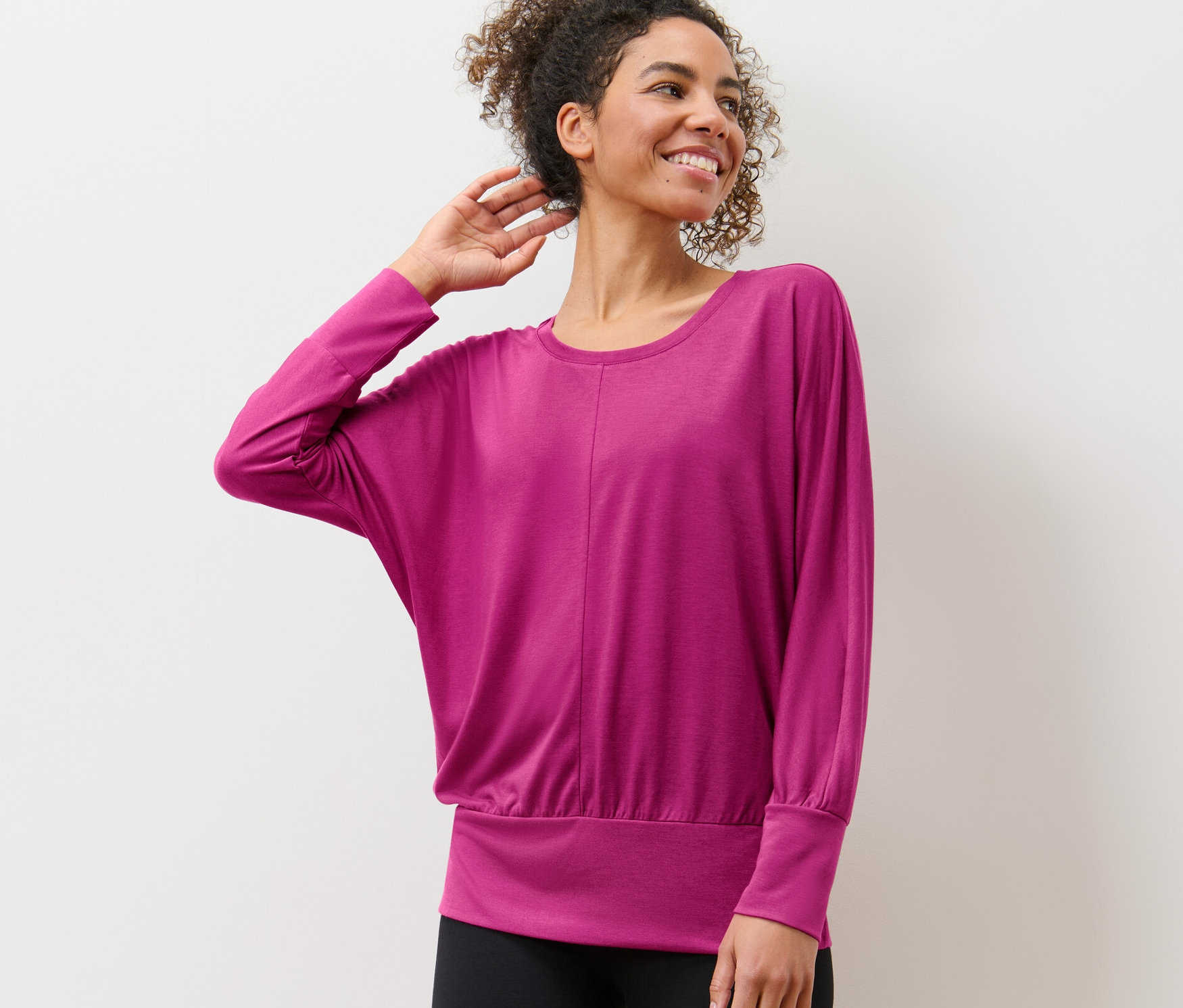 Frau posiert in Yogashirt vor einer weißen Wand.