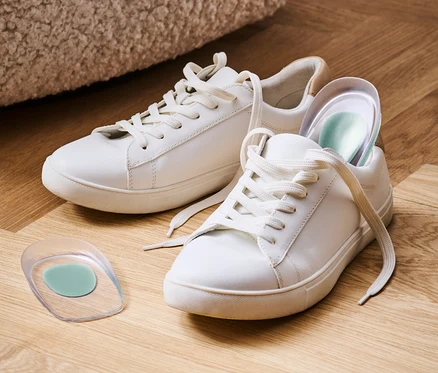 Zwei weiße Turnschuhe und ein Paar Fersenkeile auf einem Holzboden.
