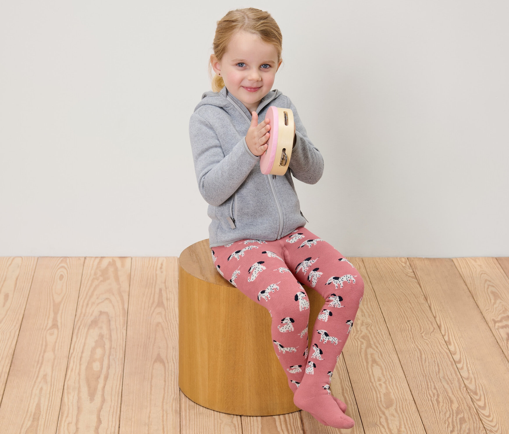 Mädchen sitzt und spielt auf einem Tamburin, trägt rosa und graue Kinder-Thermostrumpfhosen.