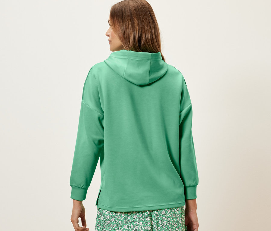 Frau von hinten trägt einen grünen Hoodie aus Modal-Mix und einen geblümten Rock.