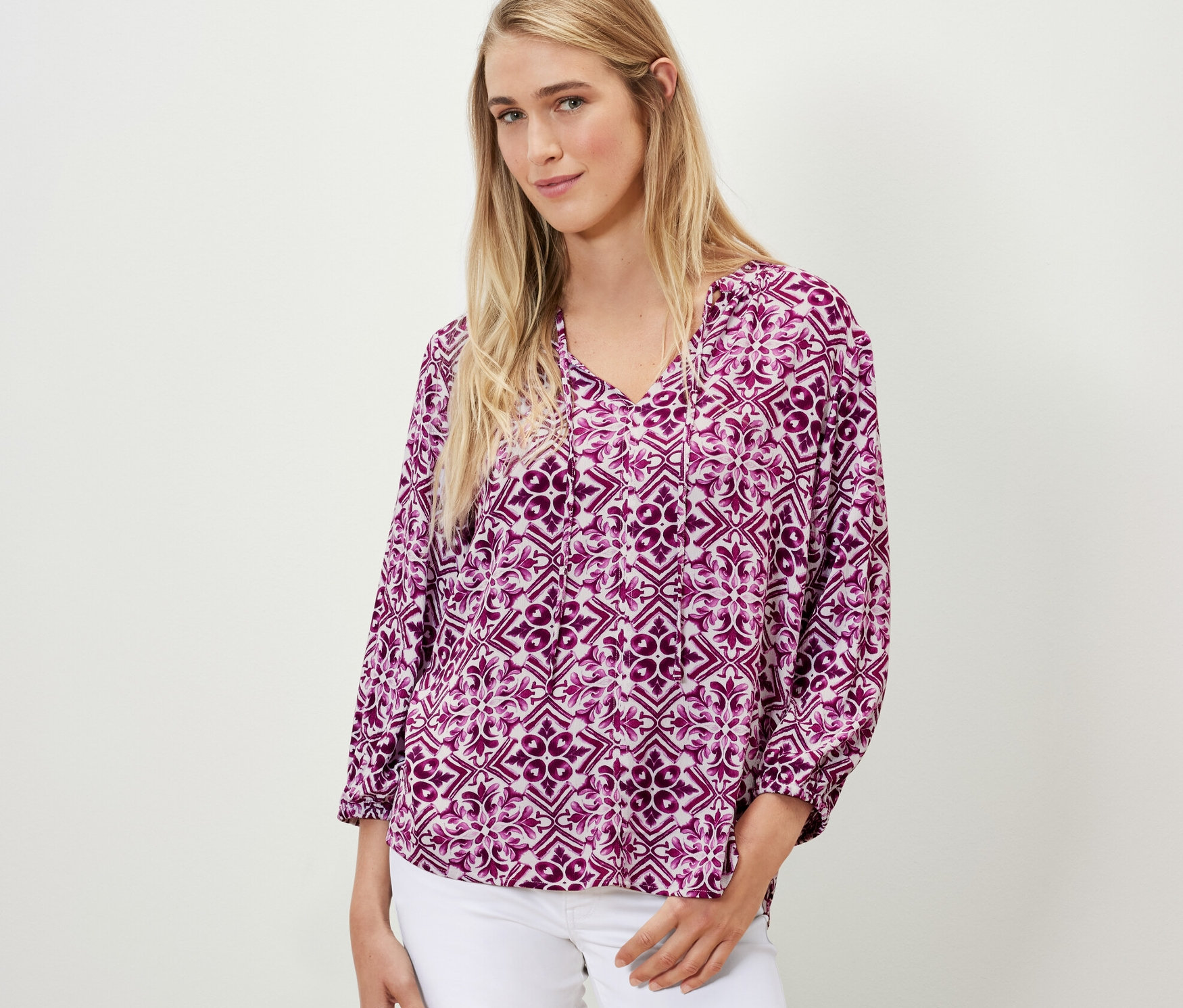 Frau trägt bedruckte Tunika-Bluse, berry und weiße Jeans.