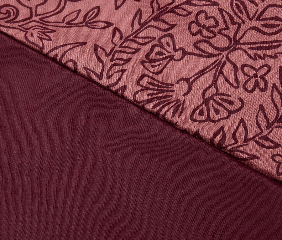 Detailaufnahme eines bordeauxfarbenen Stoffes mit Blumenmuster.