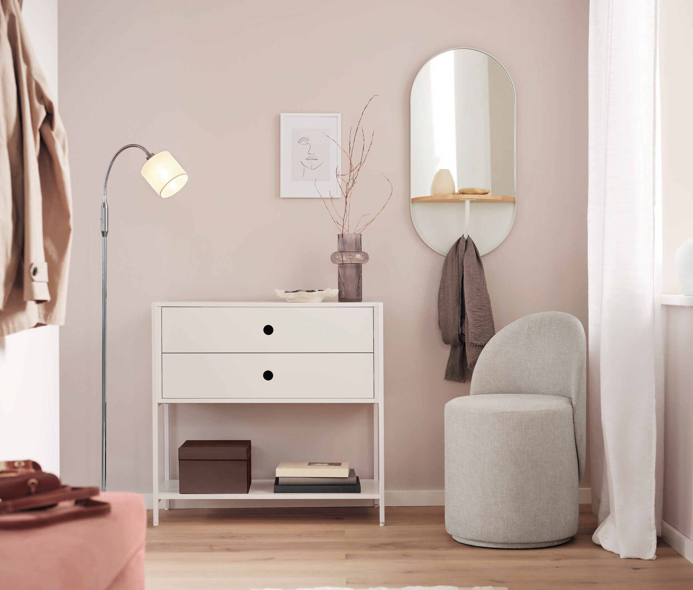 Ein weißes Sideboard mit zwei Schubladen steht neben einem Spiegel und einem grauen Hocker in einem Raum.