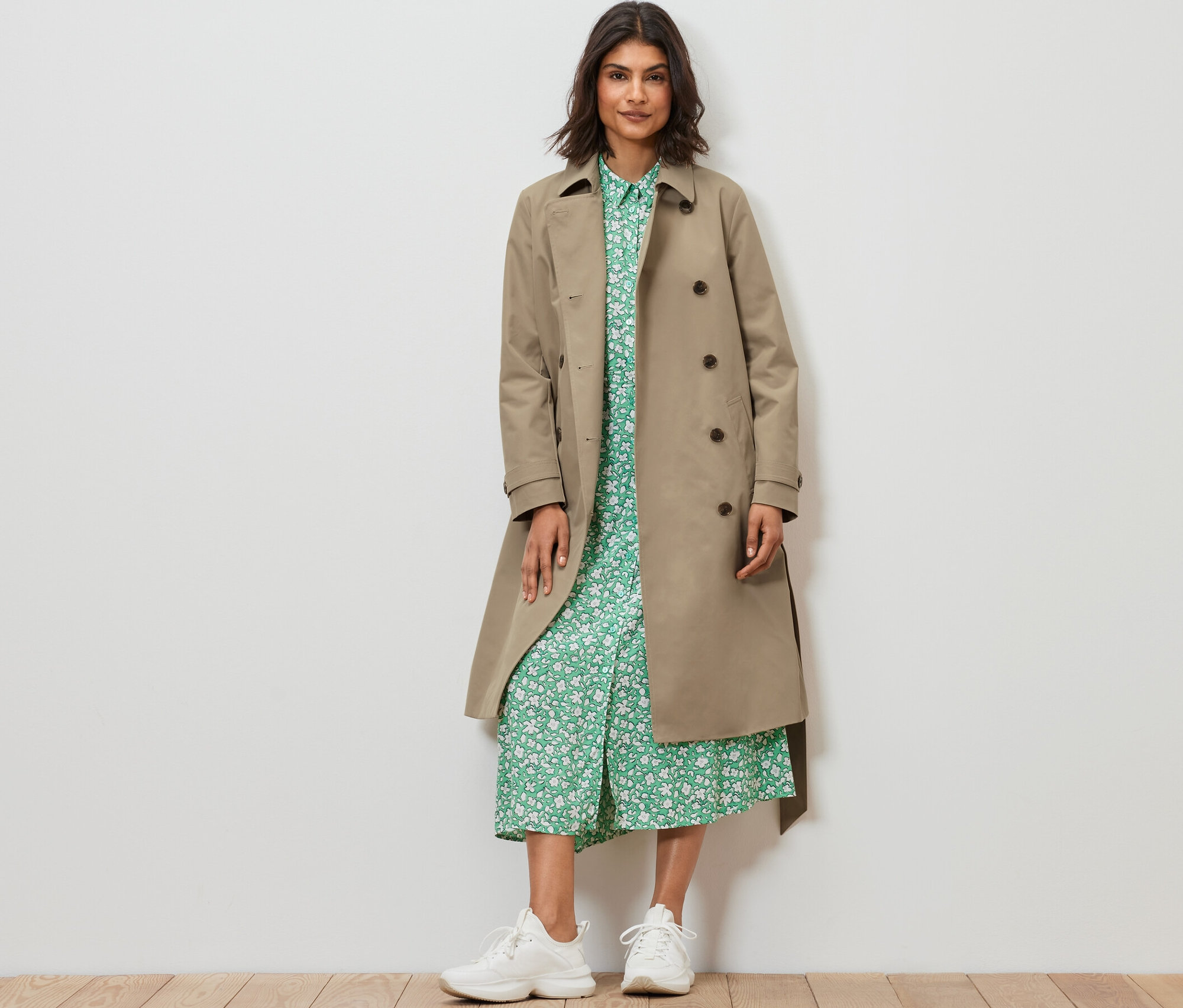 Frau steht und trägt einen Trenchcoat in Sand.