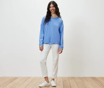 Frau steht und trägt ein hellblaues Sweatshirt.