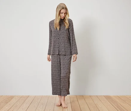 Eine Frau steht und trägt einen braunen Pyjama mit Muster.