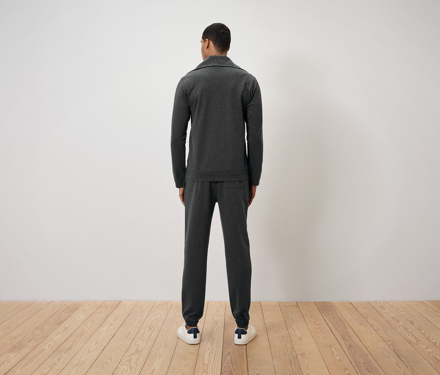 Mann von hinten trägt einen dunkelgrauen Trainingsanzug und weiße Turnschuhe.