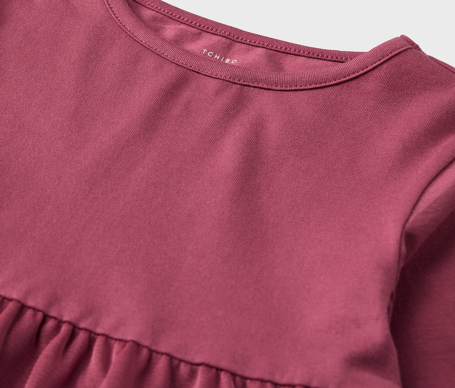 Detailaufnahme eines rosa Kleides mit Rüschenrock und Rundhalsausschnitt.