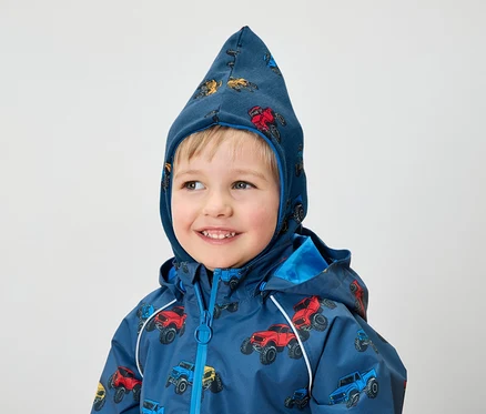 Ein lächelnder Junge trägt eine blaue Jacke und eine Kapuze mit Monster-Truck-Aufdruck.