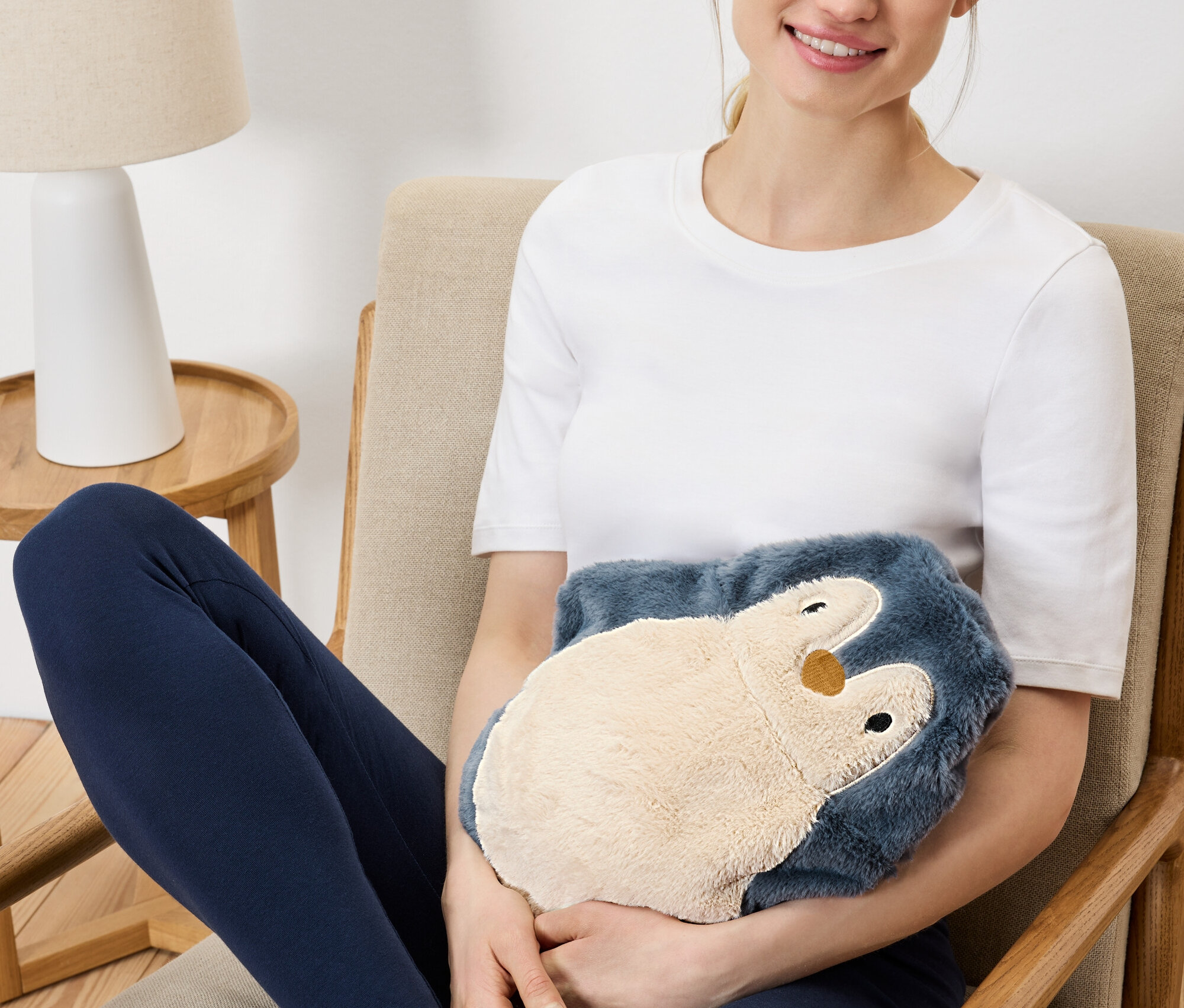 Frau sitzt im Sessel und hält ein Plüsch-Pinguin-Wärmekissen.