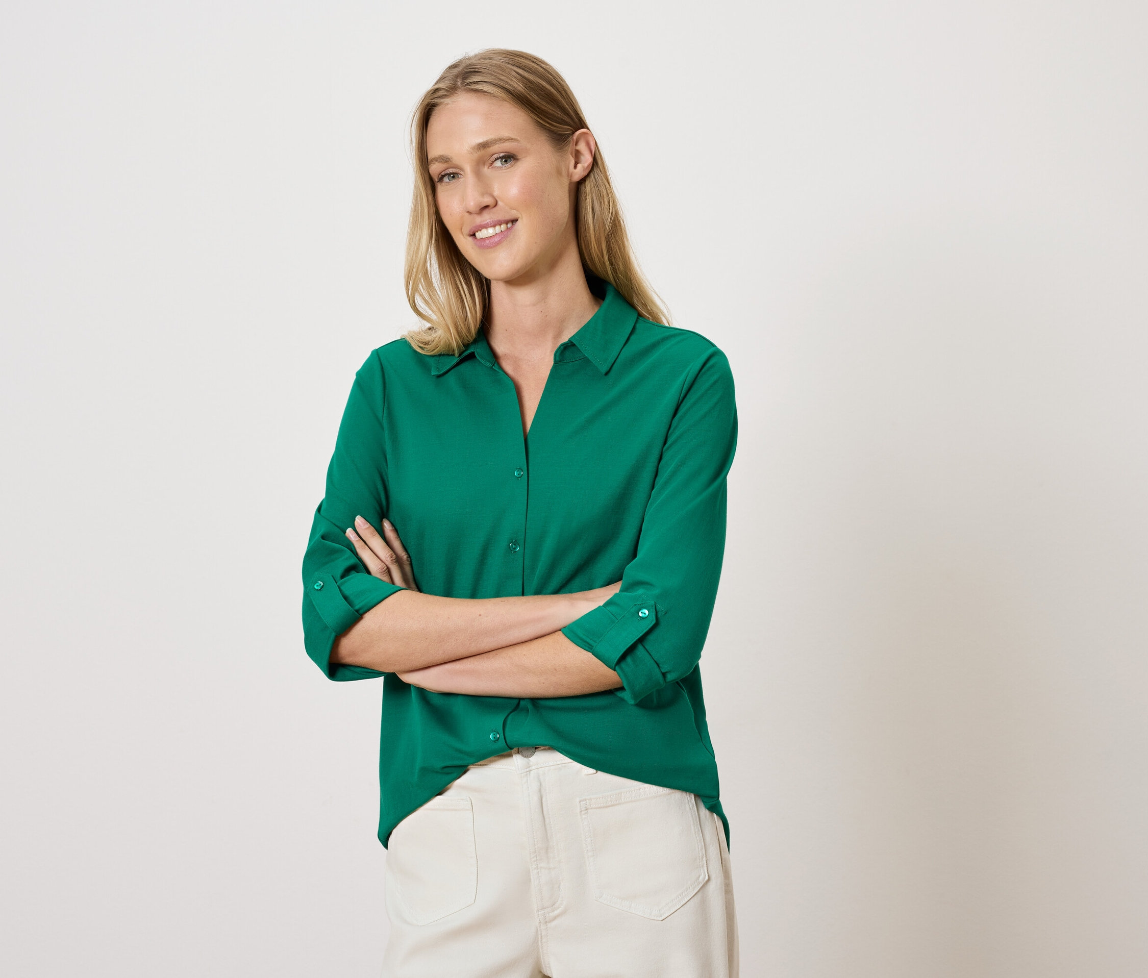 Frau posiert mit verschränkten Armen in einem grünen Hemd und einer weißen Hose.