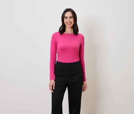 Frau mit dunklen Haaren steht und lächelt, sie trägt eine pinke Langarmbluse und eine schwarze Hose.