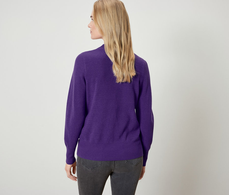 Rückansicht einer blonden Frau mit lila Pullover und grauen Jeans.