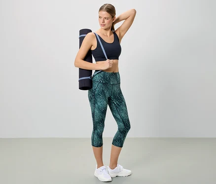 Frau in Sportbekleidung mit einer Yogamatte über der Schulter.