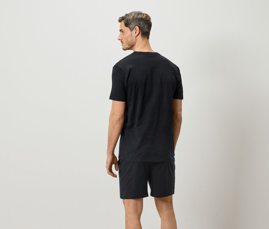 Mann von hinten, trägt schwarzes T-Shirt und Shorts vor einem weißen Hintergrund.
