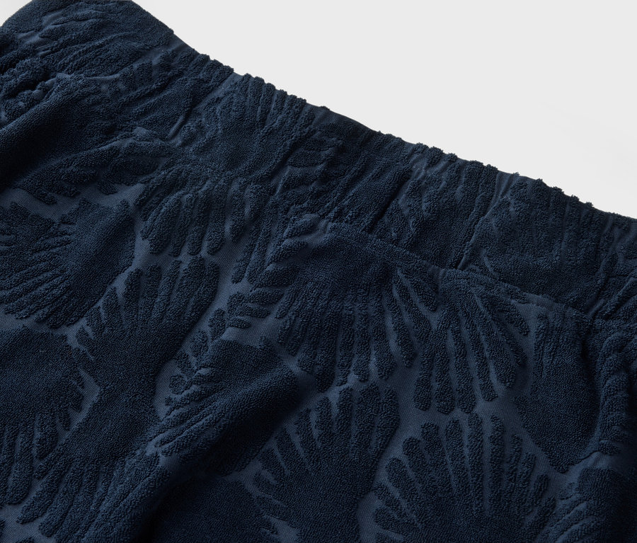Nahaufnahme der Oberseite einer marineblauen, strukturierten Hose mit elastischem Bund und Palmenmuster.