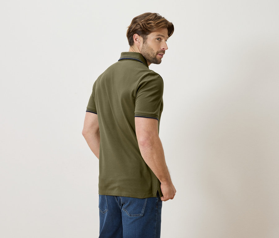 Mann von hinten in olivgrünem Poloshirt und Jeans vor hellem Hintergrund.
