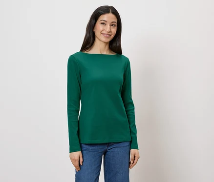 Frau trägt ein grünes Langarmshirt und Jeans vor einem weißen Hintergrund.