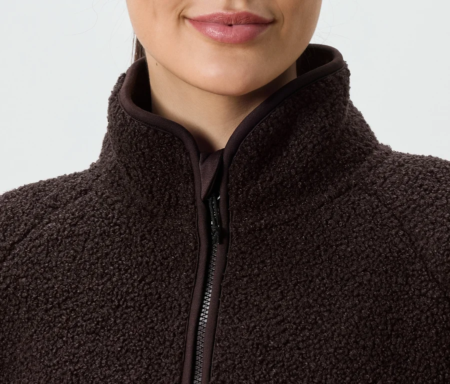 Nahaufnahme einer Frau, die eine braune Fleecejacke mit Reißverschluss und hohem Kragen trägt.