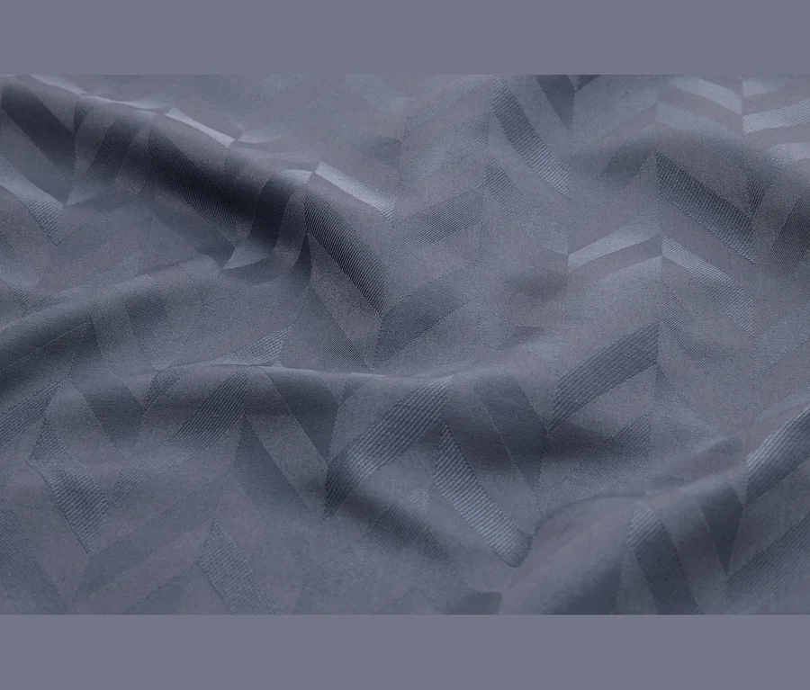 Drapierter grauer Stoff mit einem dezenten, gewebten Chevron-Muster, das durch Textur und Licht sichtbar wird.