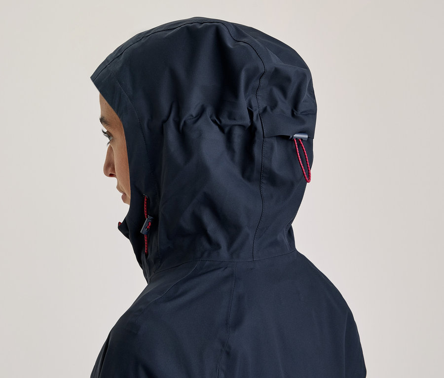 Person von der Seite, die eine dunkelblaue Kapuzenjacke mit hochgezogener Kapuze und roten Kordelzügen trägt.