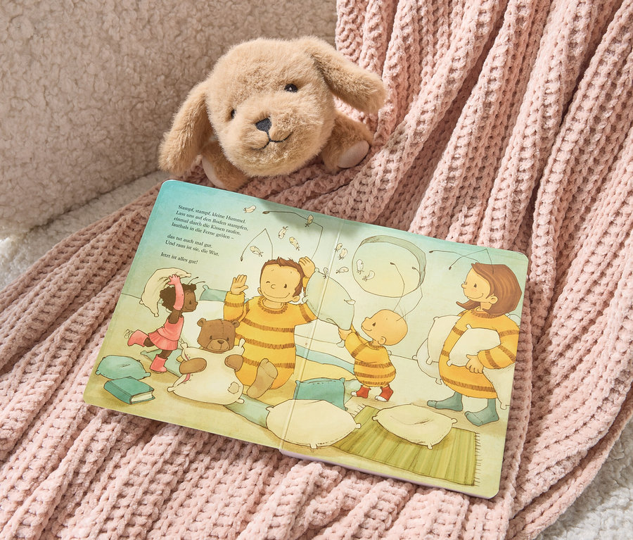 Ein Plüschhund liegt auf dem Buch "Die Baby-Hummel Bommel" und einer rosa Strickdecke.