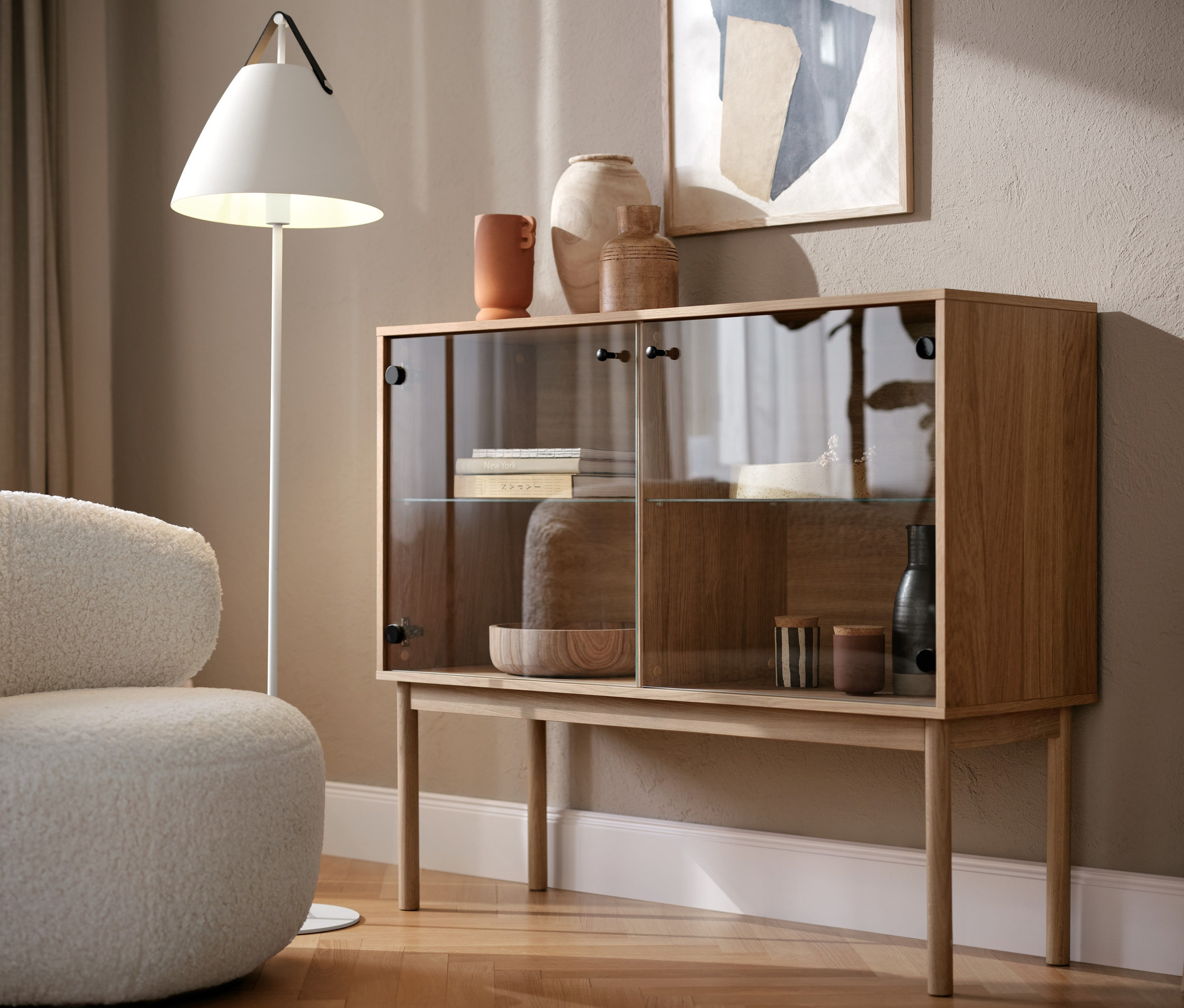 Sessel mit Drehfunktion und Glasvitrine im Wohnzimmer. Eine Stehlampe »Strap« steht daneben.