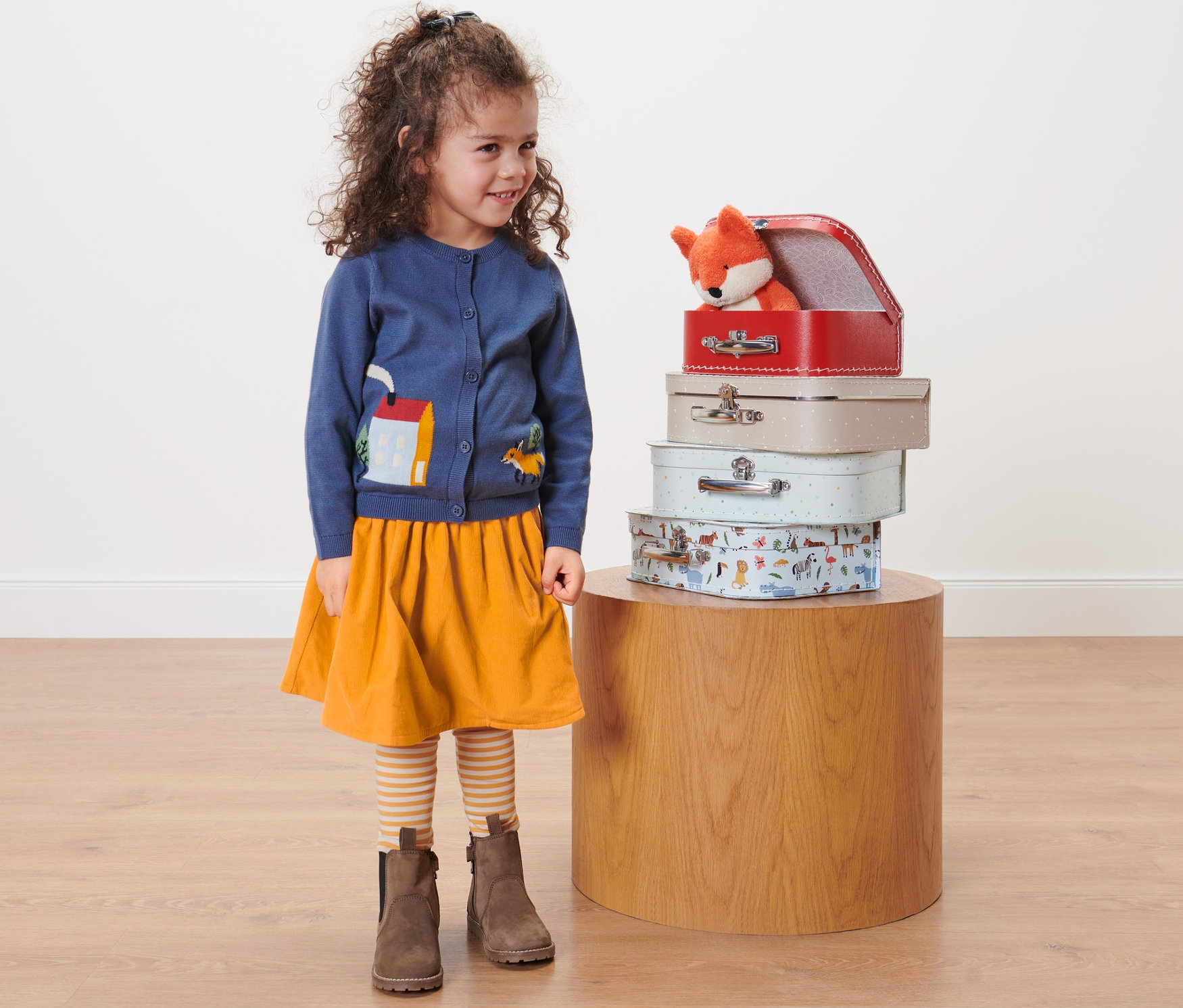Mädchen steht neben einem Stapel Koffer, trägt einen Kleinkind-Cord-Wenderock.