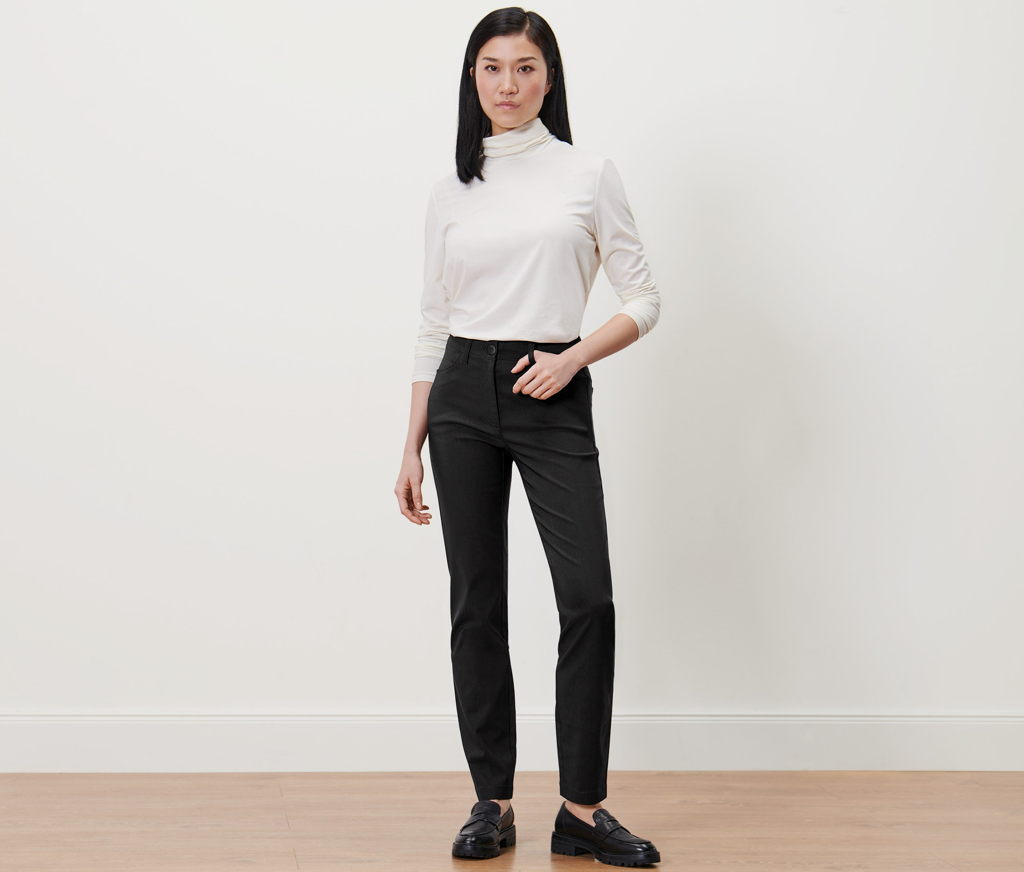 Frau trägt weißen Rollkragenpullover und schwarze Bengalin-Hose.