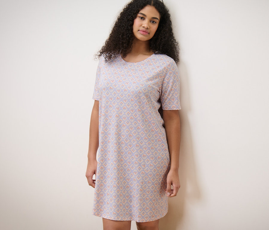 Frau im Nachthemd steht an einer Wand.