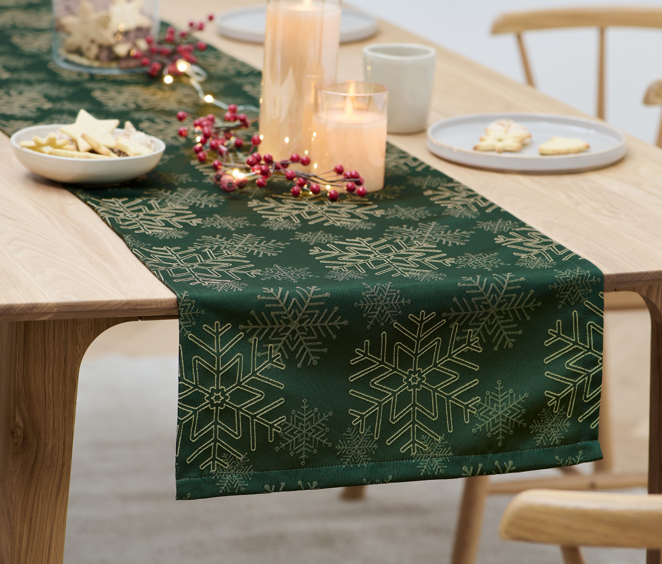 Auf einem Tisch liegt ein grüner Jacquard-Tischläufer mit Weihnachtsschmuck.