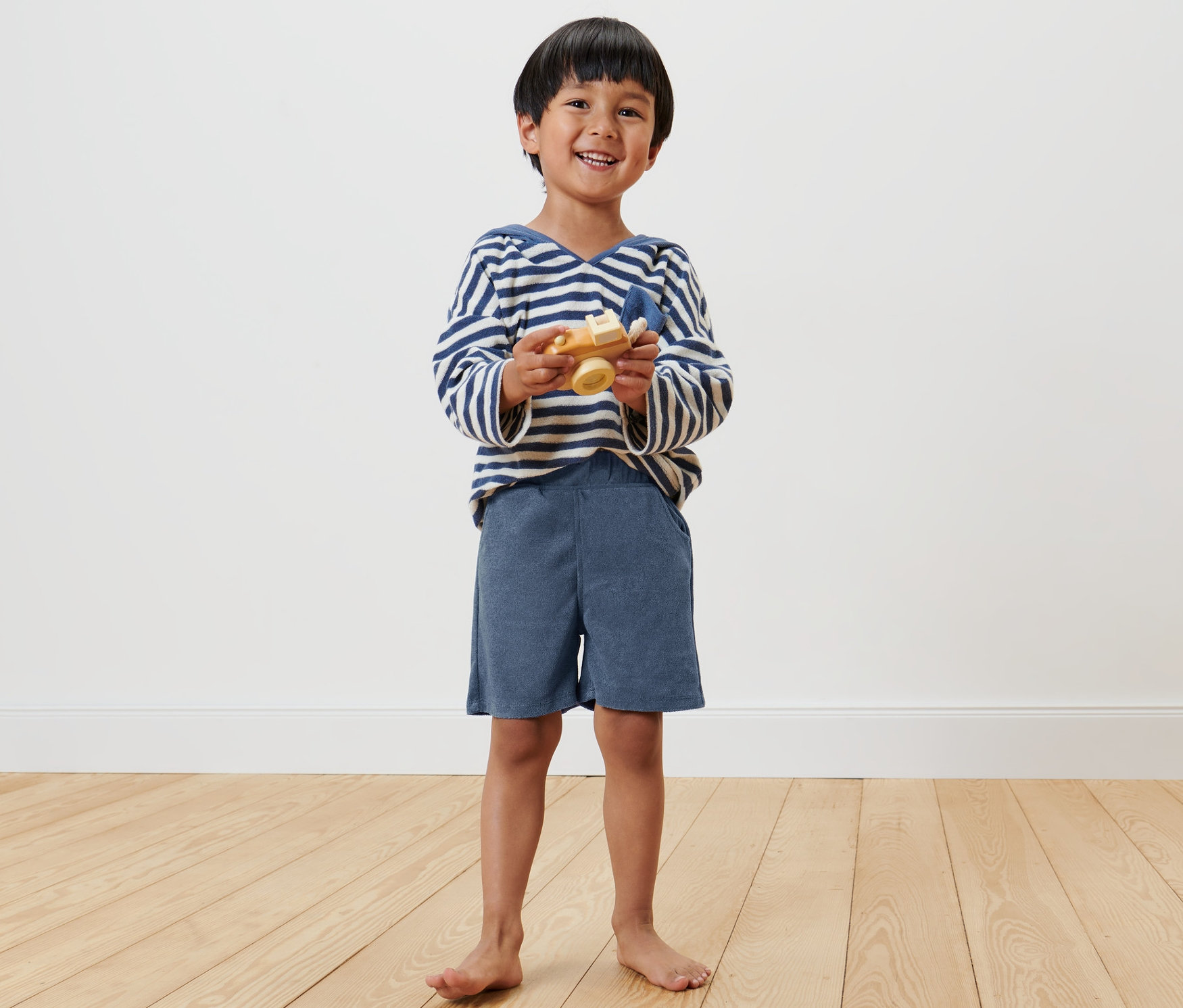 Lächelnder Junge hält ein Holzspielzeugflugzeug und trägt 2 Kinder-Shorts.