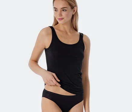 Frau trägt ein schwarzes SCHIESSER Trägertop mit Modal und dezenter Streifenstruktur sowie einen schwarzen Slip. Sie hebt das Top leicht an.